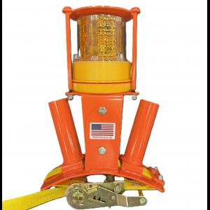 Orange industrial warning beacon with a yellow flashing light enclosed in a protective cage. The device has two angled orange mounting tubes, a ratchet-style strap mechanism at the base, and a small American flag sticker on the front. The beacon is isolated on a white background.