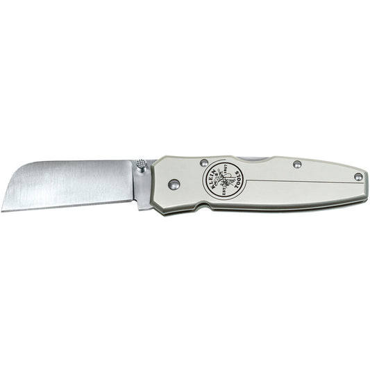 Open folding pocket knife with a satin-finish stainless steel blade and silver metal handle displayed horizontally on a light gray background. The knife features a wide rectangular blade, visible pivot hardware, and a circular logo on the handle reading “Klein Tools Est. 1857” with a lineman graphic. The blade is extended and the handle has a smooth, contoured design with several visible screws.