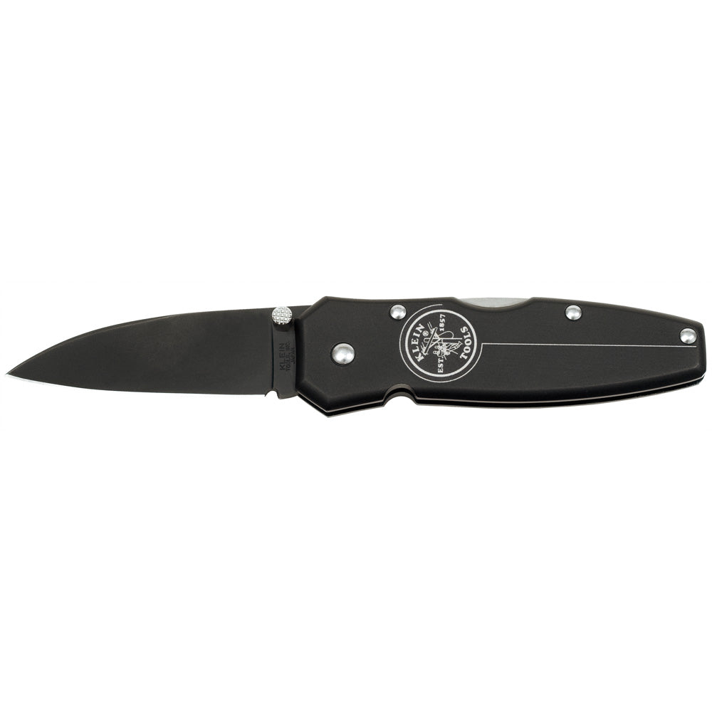 Black folding pocket knife with a matte black blade and handle, shown fully opened against a light gray background. The handle features silver screws, a thumb stud near the blade hinge, and a circular Klein Tools logo printed on the side.