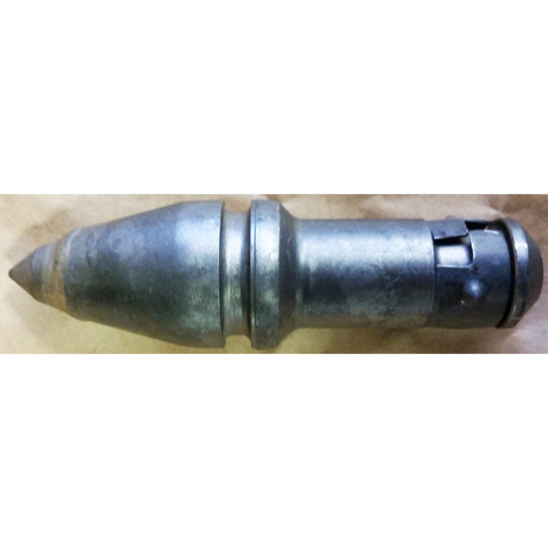 Close-up of a dark gray metal industrial cutting tool or drill bit laid horizontally on a light-colored surface. The tool has a pointed conical tip on the left, a cylindrical body with a raised collar in the middle, and a darker locking or coupling mechanism on the right end. The metal surface shows signs of wear and use.